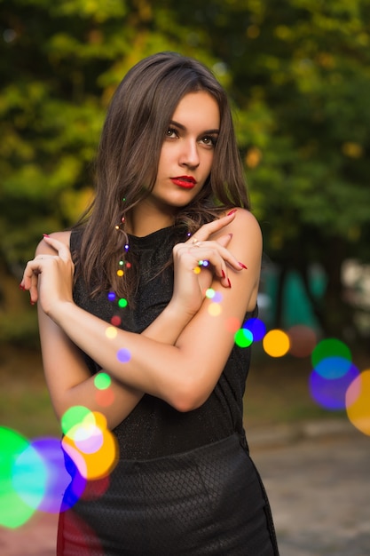 Modèle brune à la mode avec un maquillage lumineux tenant une guirlande dans le parc de la ville