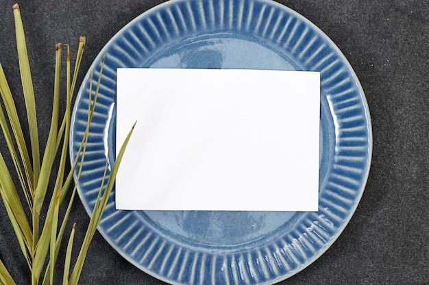 Photo modèle de carte d'invitation de mariage au-dessus d'une assiette bleue avec une feuille de palmier sur un fond grunge gris