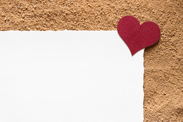 Modèle de carte postale avec coeur bordeaux sur fond de sable.