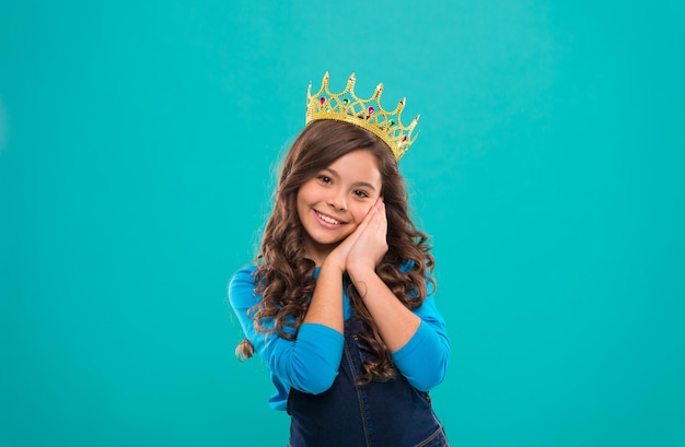 Modèle de concours de beauté L'enfant porte le symbole de la couronne d'or de la princesse Fille mignon bébé porte la couronne tout en se tenant sur fond bleu Concept de l'enfance Chaque fille rêvant de devenir princesse Dame petite princesse