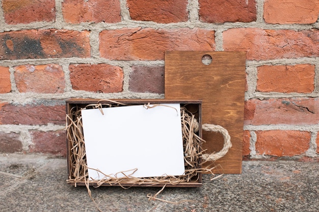 Modèle convivial de maquette de certificat de carte postale posé à l'intérieur d'une boîte-cadeau en bois sur un mur de briques