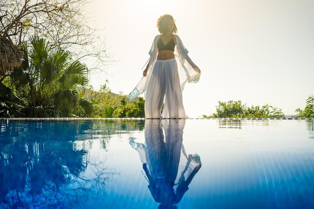 Modèle debout à côté d'une piscine tropicale extérieure