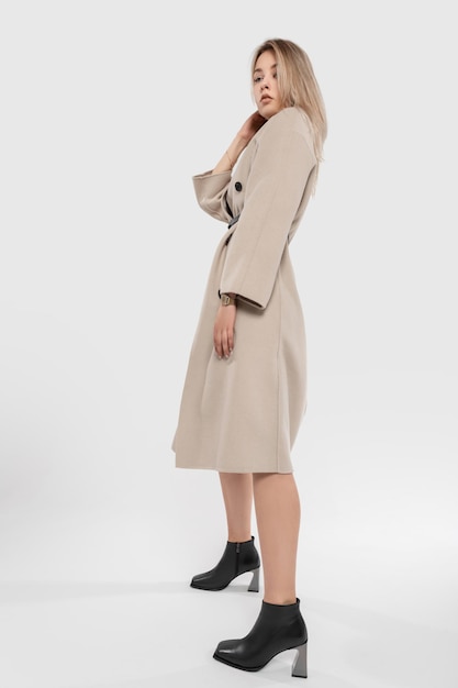 Modèle élégant belle jeune fille blonde dans un élégant manteau beige à la mode avec des chaussures en cuir classiques dans le studio