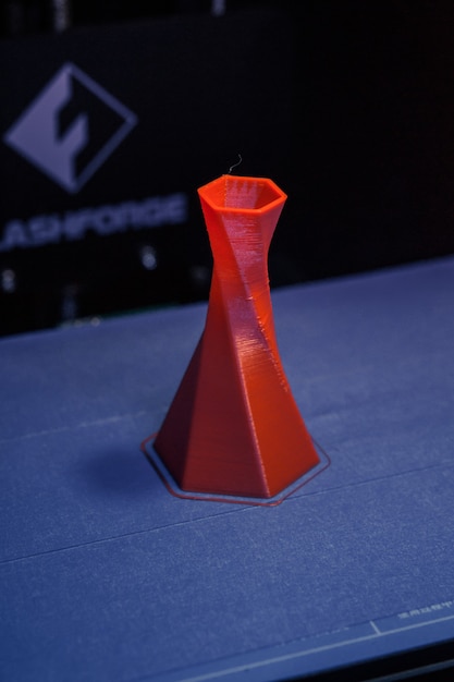 Le modèle est imprimé sur l'imprimante 3D à proximité. Imprimante 3D imprimant un objet de couleur rouge sur la base d'un gros plan de fond bleu et noir. Technologie d'impression 3D moderne