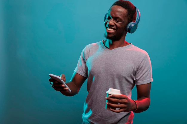 Modèle excité écoutant de la musique jouée sur un smartphone avec un casque pendant qu'il savoure une tasse de café. Personne du millénaire utilisant un casque et un téléphone portable avec un son radio pour s'amuser.