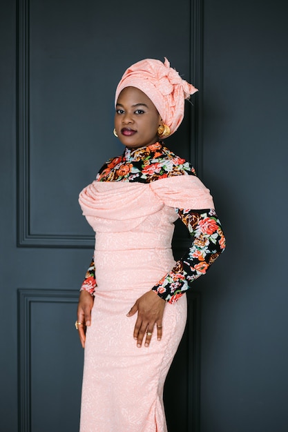 Modèle féminin africain en robe rose élégante, chemisier brillant et foulard, posant au studio