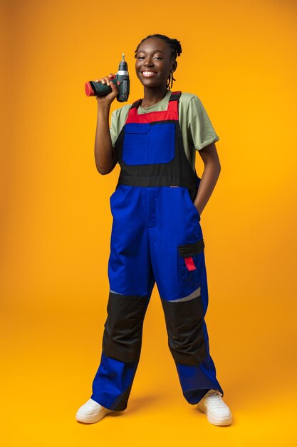 Modèle féminin afro-américain noir en uniforme tenant un outil de réparation de tournevis contre le dos jaune