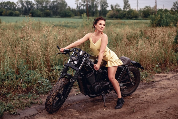 Modèle féminin attrayant aux longues jambes sexuelles dans une robe jaune assis sur une moto noire