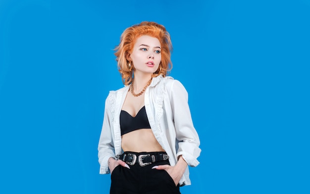 Modèle féminin aux cheveux rouges qui pose en studio sur fond bleu isolé