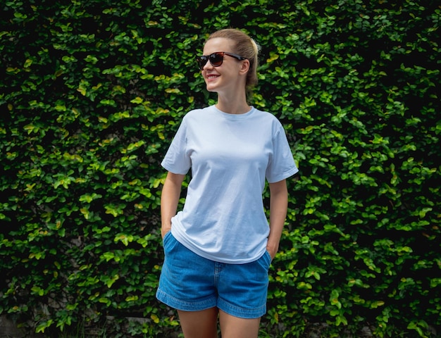 Modèle féminin portant un t-shirt blanc vierge sur le fond d'un mur de feuilles