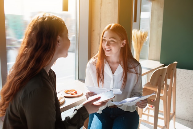 Le modèle féminin tient un document à la main. Les jeunes femmes parlent dans un café.