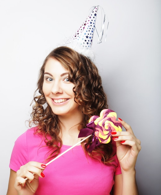 Modèle femme belle fête avec sucette, portant un chapeau en papier sur fond blanc