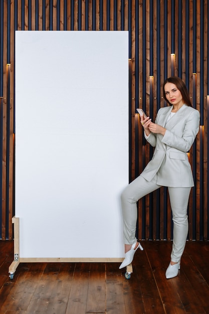 Un modèle femme en costume d'affaires avec un téléphone dans ses mains montre une toile blanche