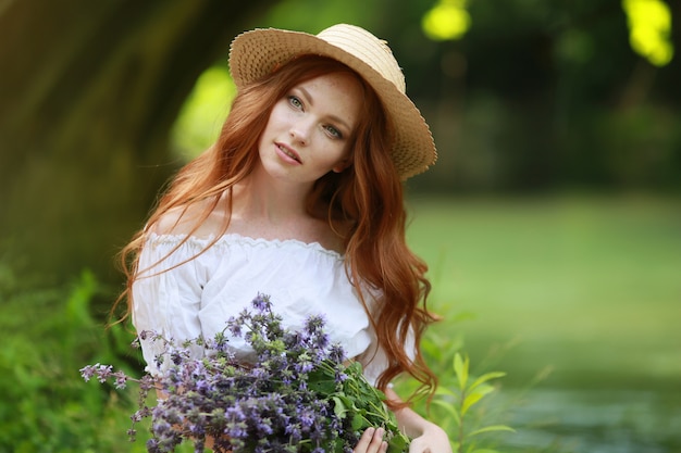 Modèle de fille élégante dans une longue robe assise sur le sol près du lac dans les bois