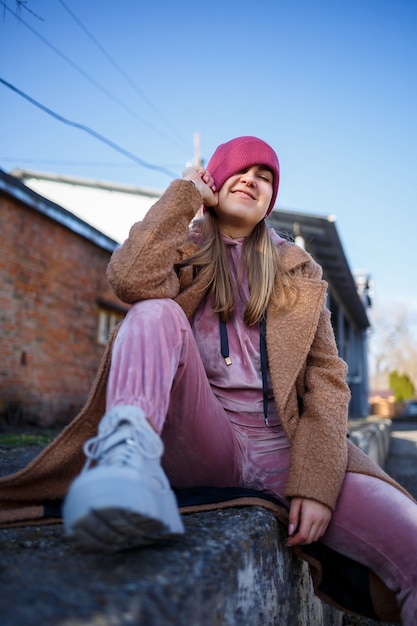 Modèle de fille élégante dans un manteau marron, un costume rose et des bottes grises sur les ruines de la ville. Les tendances de la mode moderne. Image à la mode