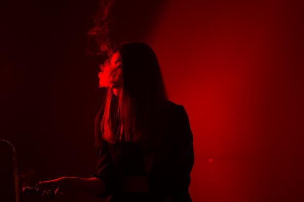 Le modèle de fille fume la vape à la lumière rouge.