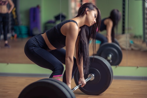 Modèle de fitness féminin athlétique tenant des haltères lourds et se préparant au soulevé de terre.