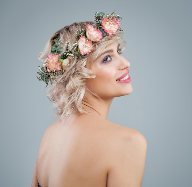 Modèle heureux en portrait de fleurs Belle femme aux cheveux bouclés blonds courts et maquillage sur fond bleu