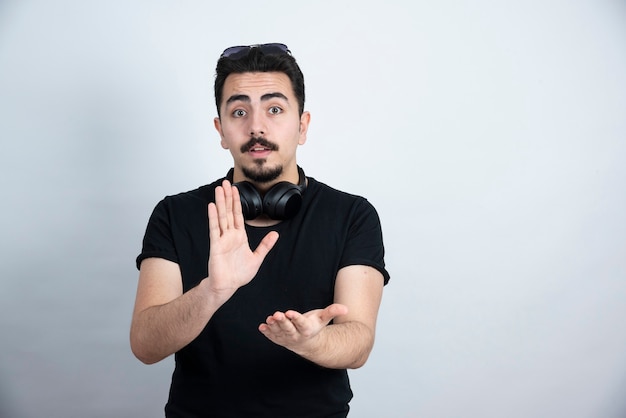 Modèle homme brune debout dans les écouteurs et applaudissant contre le mur blanc.