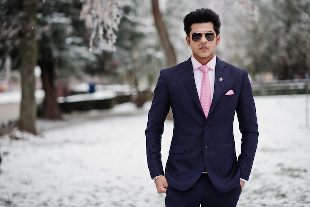Modèle d'homme macho indien élégant en costume et lunettes de soleil cravate rose posés le jour de l'hiver