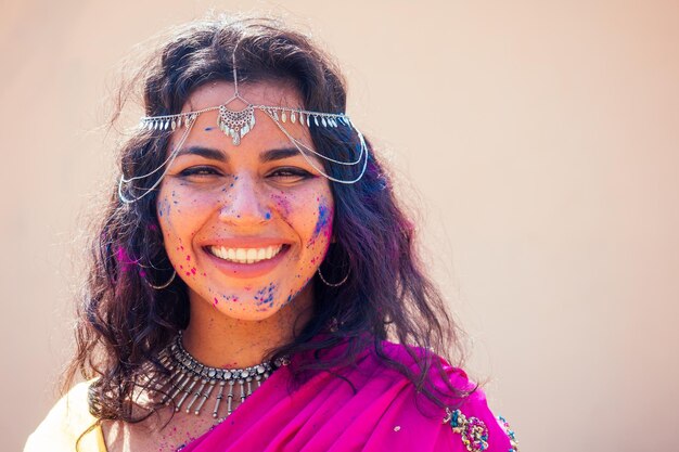 Modèle indien féminin blanc neige sourire sur le festival de couleur holiFemme indienne en robe sari traditionnelle avec des cheveux bouclés noirs dans une peinture rose et bleue et des bijoux bindi célébrant le festival de couleur Holi