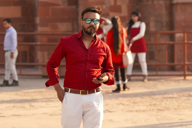 Modèle indien intelligent en chemise rouge regardant avec un téléphone portable à la main