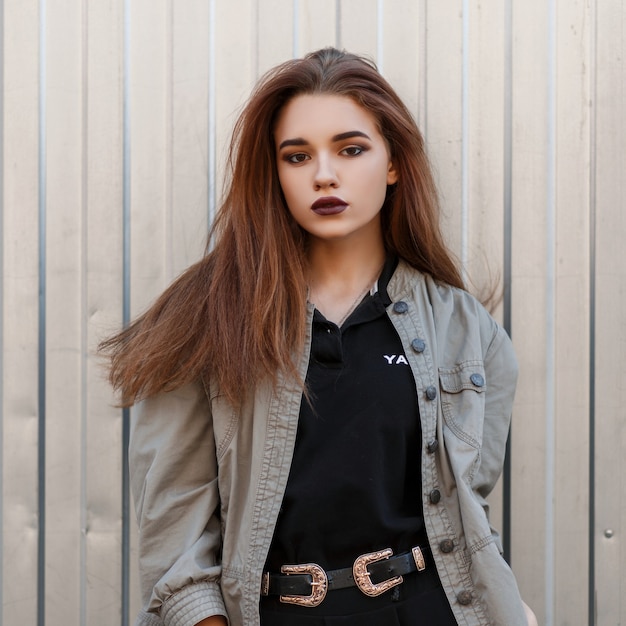 Modèle de jeune femme aux lèvres sombres dans une veste à la mode et polo noir près de la paroi métallique