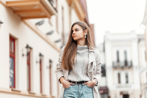 Modèle d'une jeune femme dans un trench-coat et un pull vintage tricoté marche dans la rue