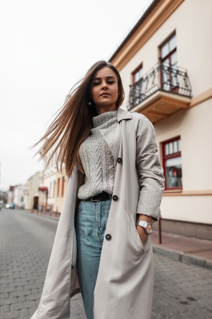 Modèle d'une jeune femme dans un trench-coat et un pull vintage tricoté marche dans la rue
