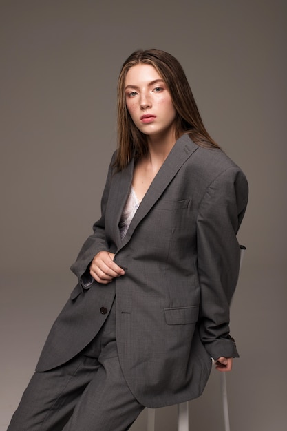 Modèle de jeune fille en costume gris homme assis sur une chaise