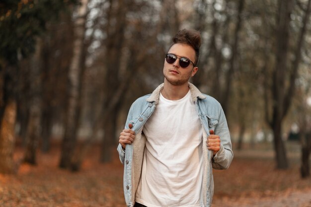 Modèle de jeune homme dans une veste bleue denim élégante posant dans le parc