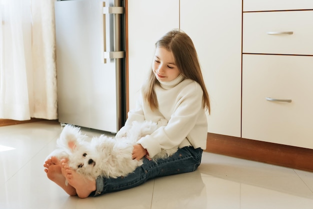 modèle joue avec animal de compagnie chien blanc écolière maltaise à la maison style de vie dans la cuisine beige