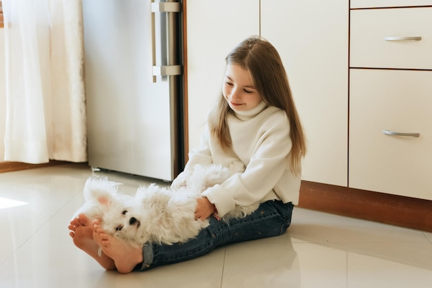 modèle joue avec animal de compagnie chien blanc écolière maltaise à la maison style de vie dans la cuisine beige