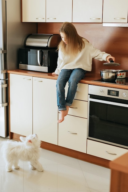modèle joue avec animal de compagnie chien blanc écolière maltaise à la maison style de vie dans la cuisine beige