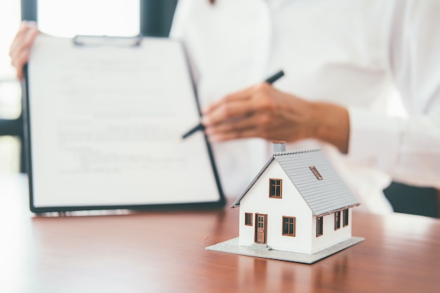 Modèle de maison avec agent immobilier et client discutant d'un contrat d'achat de maison, d'assurance ou de prêt immobilier.