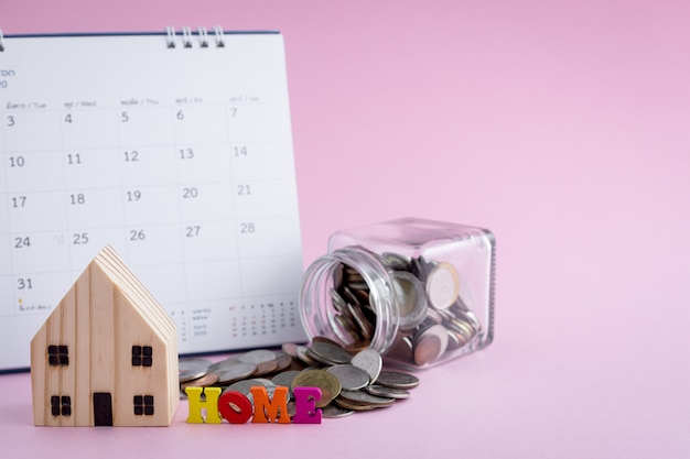 Photo modèle de maison en bois avec alphabet home, pièces d'argent dans le bocal en verre et calendrier sur fond rose pour le logement et le concept de planification