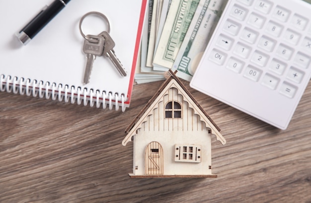 Modèle de maison en bois avec clés, calculatrice, argent, stylo et bloc-notes.