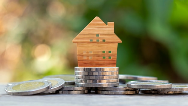 Modèle de maison en bois sur pile de pièces et fond de nature verte floue, investissement immobilier et concept de prêt immobilier.