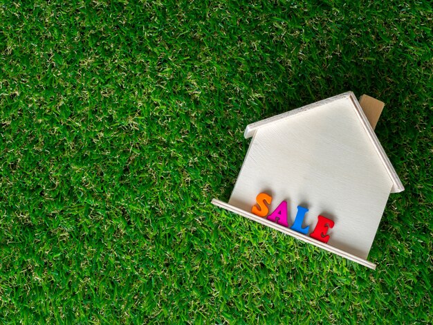 Modèle de maison en bois placé sur une pelouse verte et vente de texte coloré sur la maison