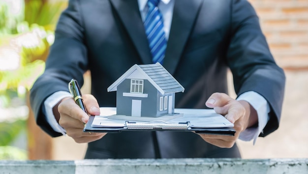 Modèle de maison dans la main de l'agent immobilier et expliquer le contrat commercial louer acheter un prêt hypothécaire ou une assurance