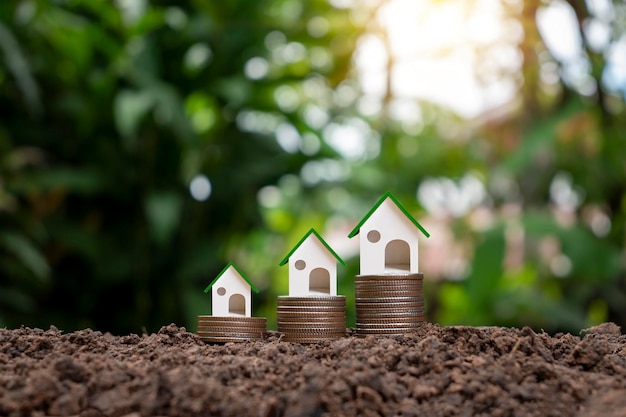 Modèle d'une maison fictive sur un tas de pièces de monnaie et fond vert naturel flou