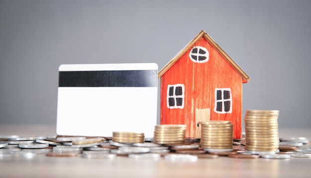 Modèle de maison, pièces de monnaie et carte de crédit sur la table en bois.