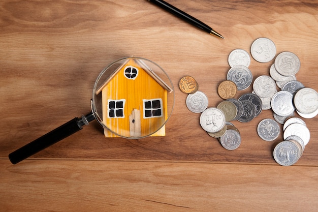 Modèle de maison, pièces de monnaie et loupe sur table en bois