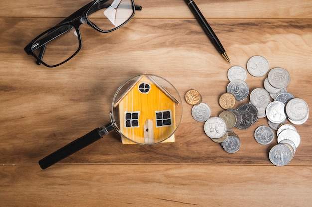 Modèle de maison, pièces de monnaie et loupe sur table en bois