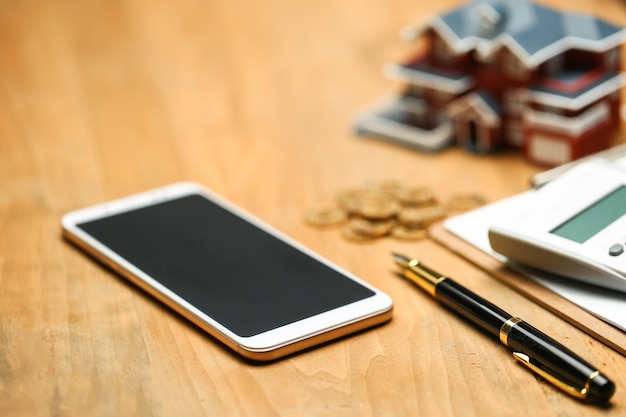 modèle de maison, smartphone, calculatrice et pièces d&#39;or sur table en bois