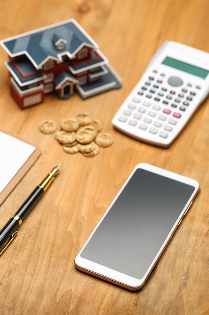 Photo modèle de maison, smartphone, calculatrice et pièces d'or sur table en bois