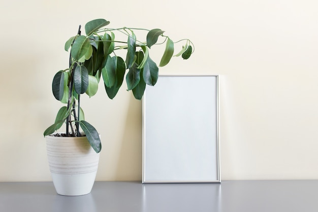 Modèle de maquette avec un cadre argenté A4 debout à côté du mur avec une plante décorative en pot