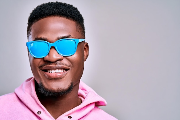 Modèle masculin afro-américain sexuel posant dans des lunettes de soleil bleues et souriant joliment coiffure courte