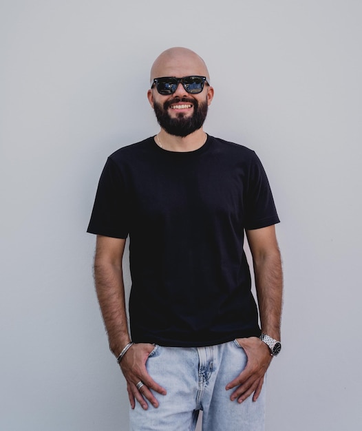 Photo modèle masculin avec barbe portant un t-shirt blanc noir sur le fond d'un mur blanc