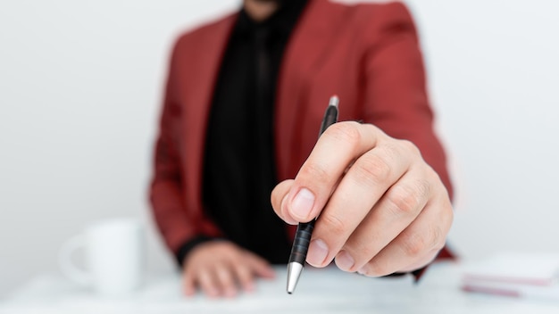 Modèle masculin en costume rouge assis à une table blanche et pointant avec un stylo sur un message important Monsieur montrant une annonce critique Tasse à café sur le pont